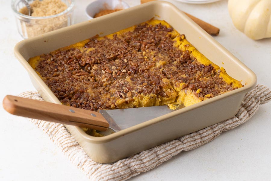 Angled shot of the casserole dish with a spatula lifting a slice of the keto sweet potato casserole, revealing its creamy texture and golden brown topping.