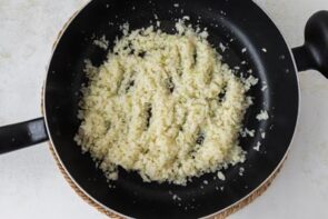 Cauliflower rice sautéing in a black nonstick skillet.