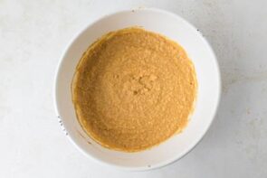 A mixing bowl filled with a blended orange pumpkin-cauliflower batter.