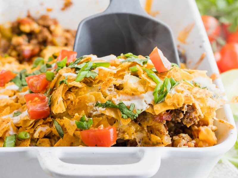 a spoon digging into a taco casserole topped with crushed chips