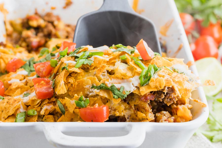 a spoon digging into a taco casserole topped with crushed chips