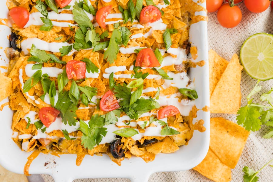 a mexican casserole in a baking dish next to keto tortilla chips and a half a lime