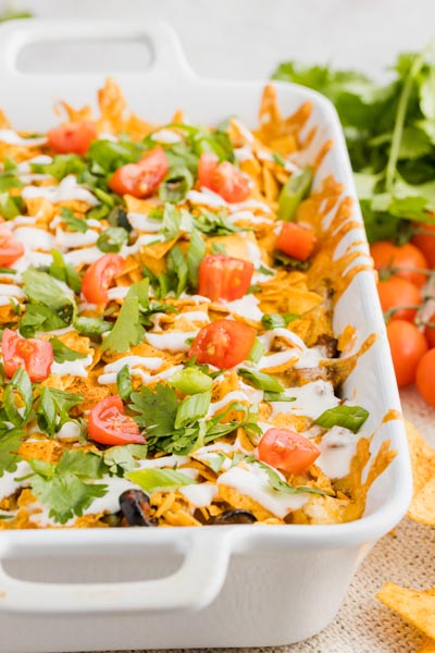 a casserole dish filled with cheesy taco casserole and topped with diced tomato and cilantro