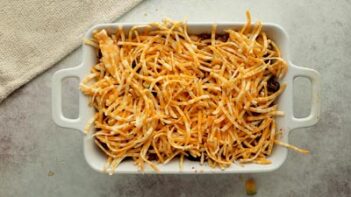 a white baking dish with a casserole topped with shredded cheese