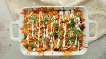 a baked casserole topped with chips, cilantro and sour cream