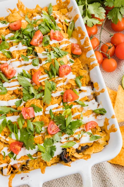 a crunchy taco casserole with green onion slices, cilantro and tomatoes next to cherry tomatoes on the vine