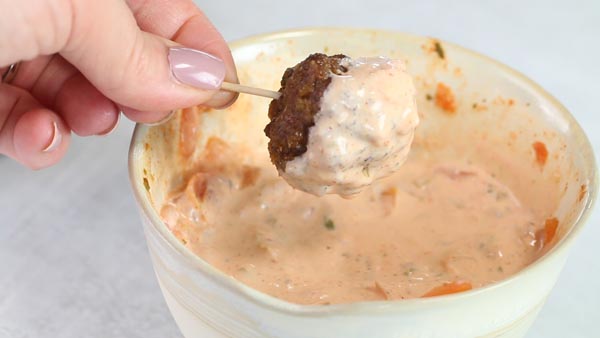 dipping taco meatball in a creamy salsa sauce with a toothpick