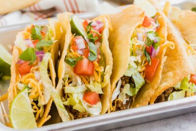 a plie of tacos on a tray topped with chopped tomatoes, red onion and cilantro