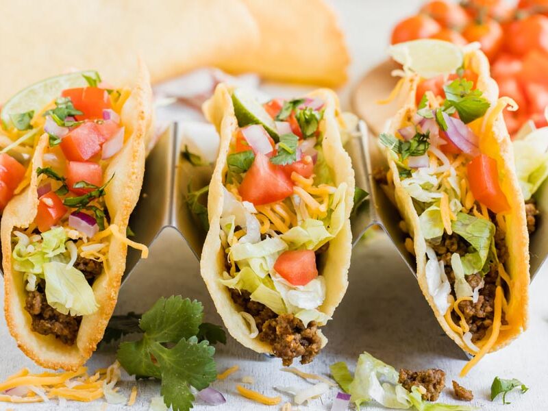 three ground beef tacos in a taco holder topped with cheese, shredded lettuce and tomato