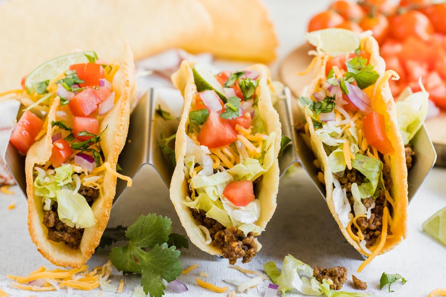 three ground beef tacos in a taco holder topped with cheese, shredded lettuce and tomato