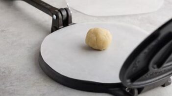 a round ball on a circle of parchment paper in a tortilla press