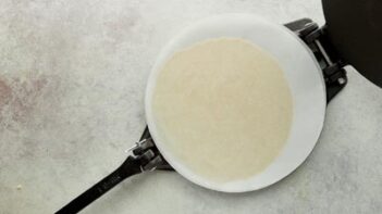 a flatten tortilla in a tortilla press with parchment paper on top