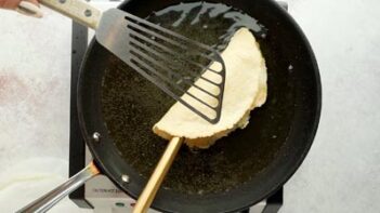 frying a taco in a skillet of oil and holding the taco folded with two spatulas