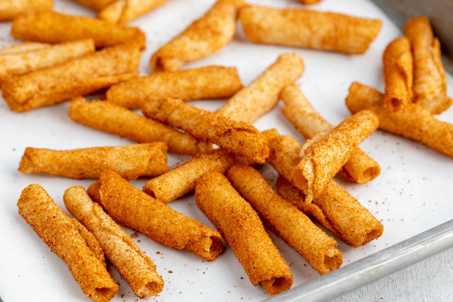 a pile of orangish red taki chips on a parchment lined baking tray