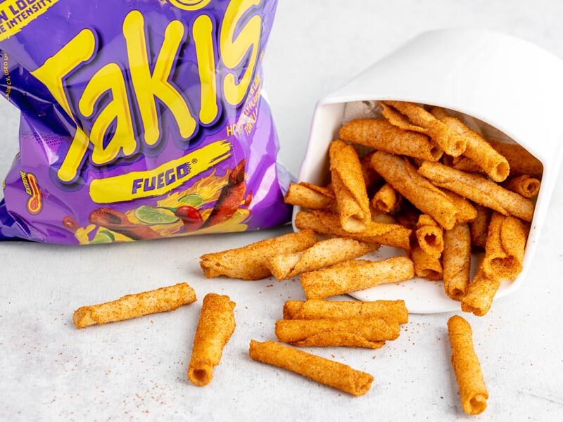a bunch of takis spilling out of a white container with a purple bag of takis next to it