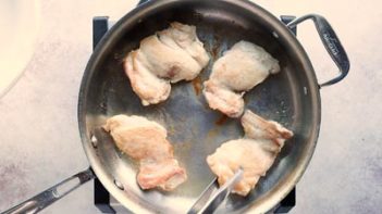 four skinless, boneless chicken thighs cooking in a stainless steal skillet