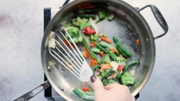 stirring vegetables in a skillet with a slotted spatula