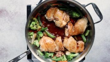 chicken thighs and vegetables cooking in a skillet with thick amber colored teriyaki sauce