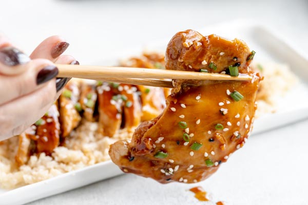 holding a teriyaki glazed chicken thigh with chopsticks