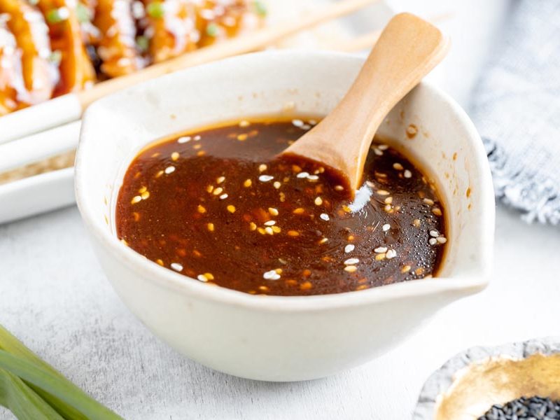 a wooden spoon sitting in a beige bowl with brown sauce in it