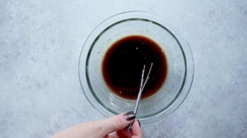 whisking teriyaki sauce ingredients in a clear bowl with a small whisk