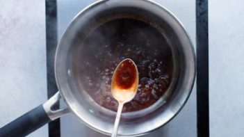a silver spoon hold with teriyaki sauce in it over a sauce pan of simmering sauce