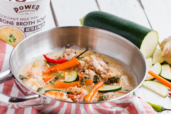 a bowl of low carb thai chicken soup next to a carton of power provisions soup