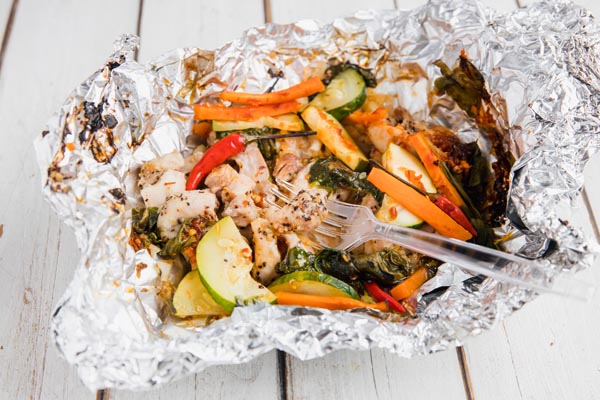 eating a camping grilled foil packet filled with chicken and vegetables with a plastic fork