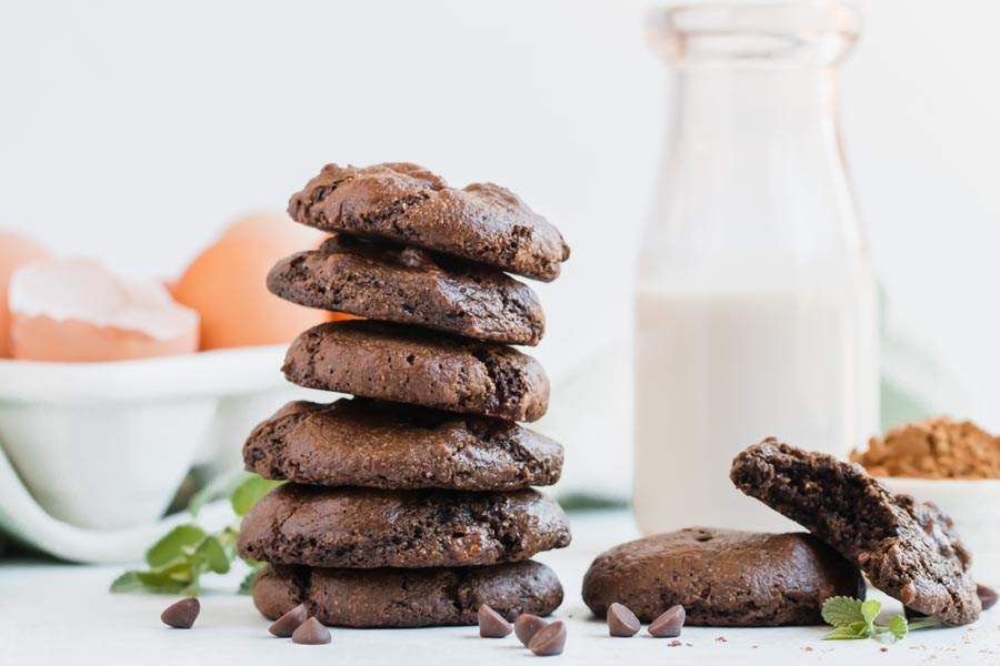a stack of chocolate cookies with eggs in the background and a glass of milk
