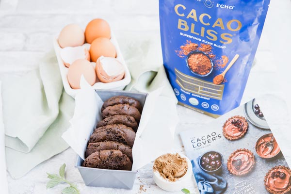 chocolate mint cookies in a loaf pan with cocoa powder, a recipe book and cracked eggs nearby