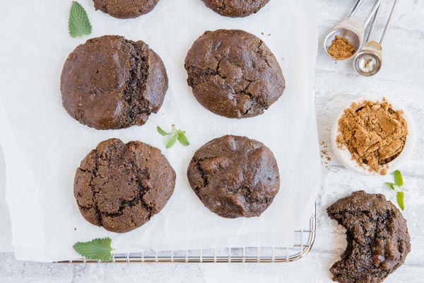 cookies on a wire tray with measuring spoons, cocoa powder and mint sprigs near