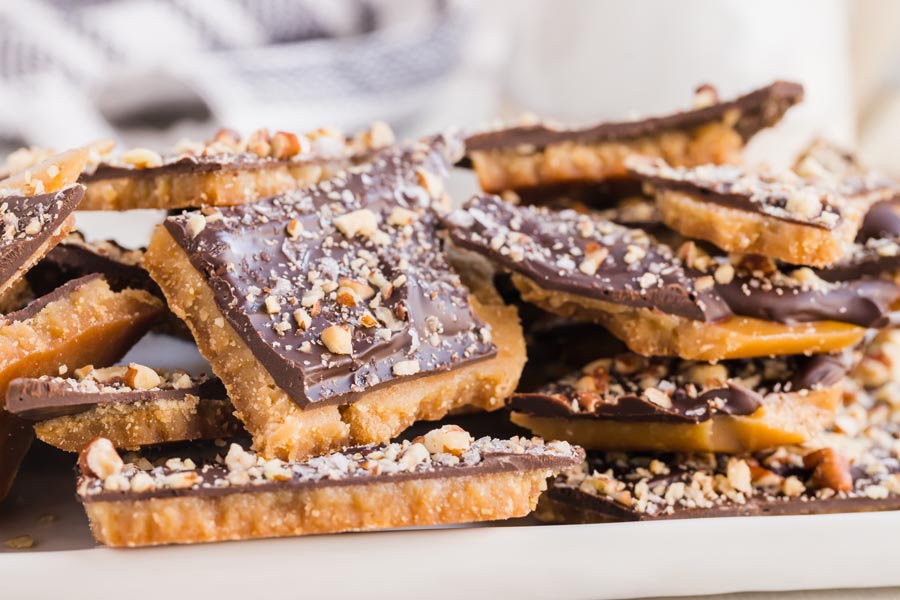 Chocolate covered toffee topped with crushed nuts on a plate stacked up tall.