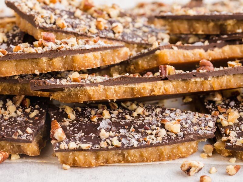 A stack of chocolate covered toffee with nuts sprinkled around.