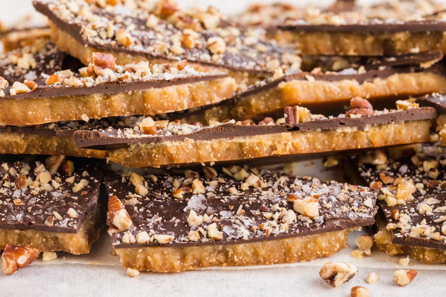 A stack of chocolate covered toffee with nuts sprinkled around.