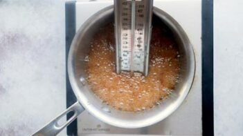 A candy thermometer inside a saucepan with bubbled caramel mixture.