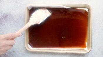Spreading toffee mixture in a baking tray with a spatula.