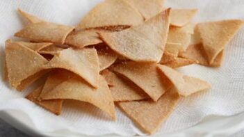 sprinkling salt on a pile of chips laying on a paper towel lined plate