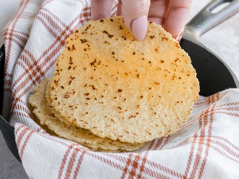 A handing holding a tortilla over a castiron skillet.
