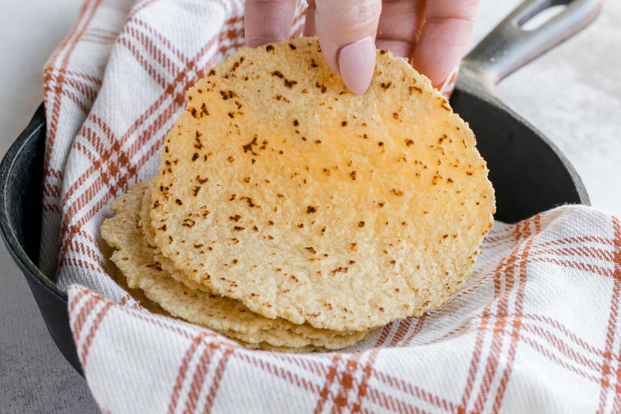 A handing holding a tortilla over a castiron skillet.