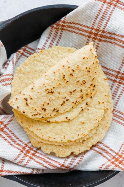 Looking down onto a lightly grilled tortillas folded and sitting on a cloth checkered orange and cream towel.