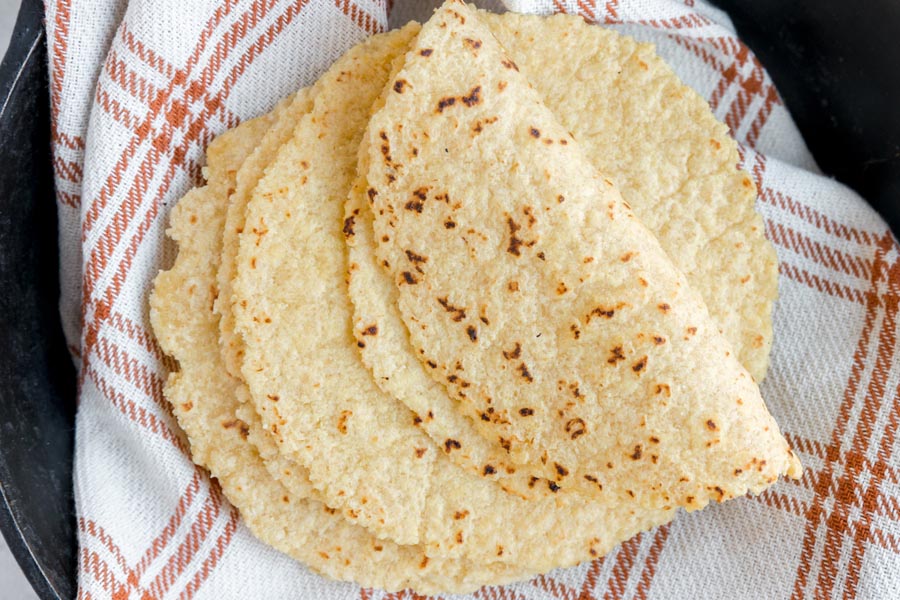 A pile of soft tortillas on an orange and cream plaid towel.