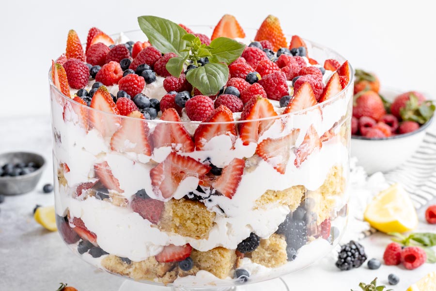 layers of berries, whipped cream and cake in a trifle bowl with berries in the background