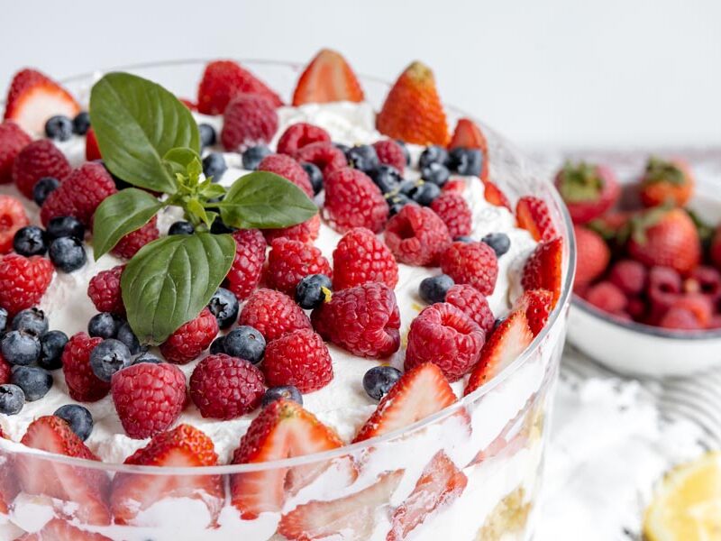 a bunch of raspberries, blueberries and strawberry slices cover the top of a whipped cream covered cake