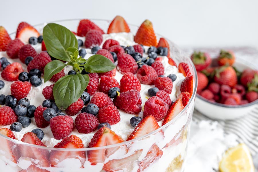 a bunch of raspberries, blueberries and strawberry slices cover the top of a whipped cream covered cake