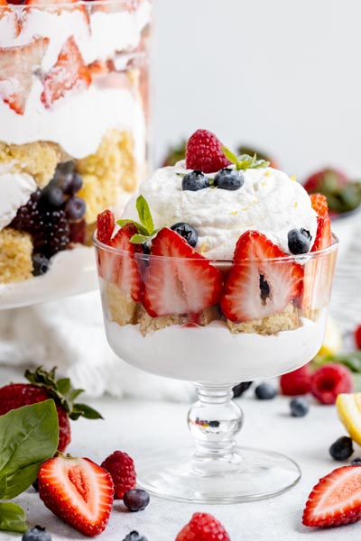 a smaller trifle dish sits in front of a large dish with fruit surrounding the dish