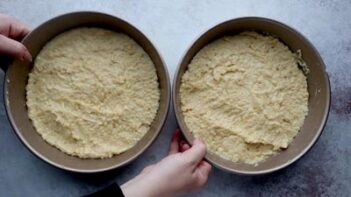 holding onto two cake pans filled with cake batter