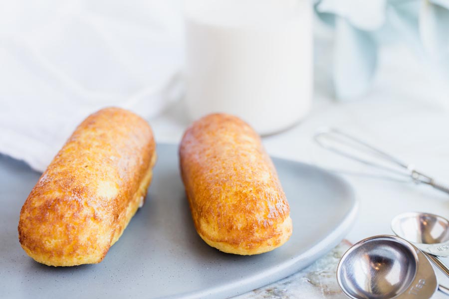 two twinkies on a gray plate next to measuring spoons and a whisk