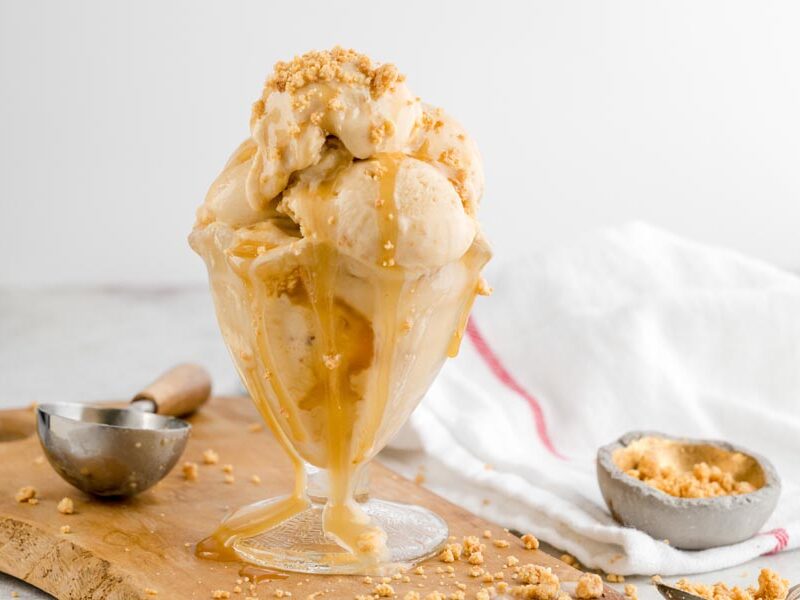Keto Twix ice cream served in a glass sundae dish with caramel sauce dripping down the sides and cookie crumbles scattered around.