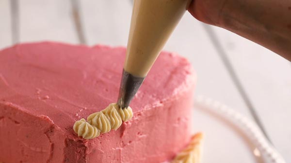 piping white frosting stars along a cake