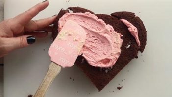 spreading pink frosting on a chocolate cake with a spatula